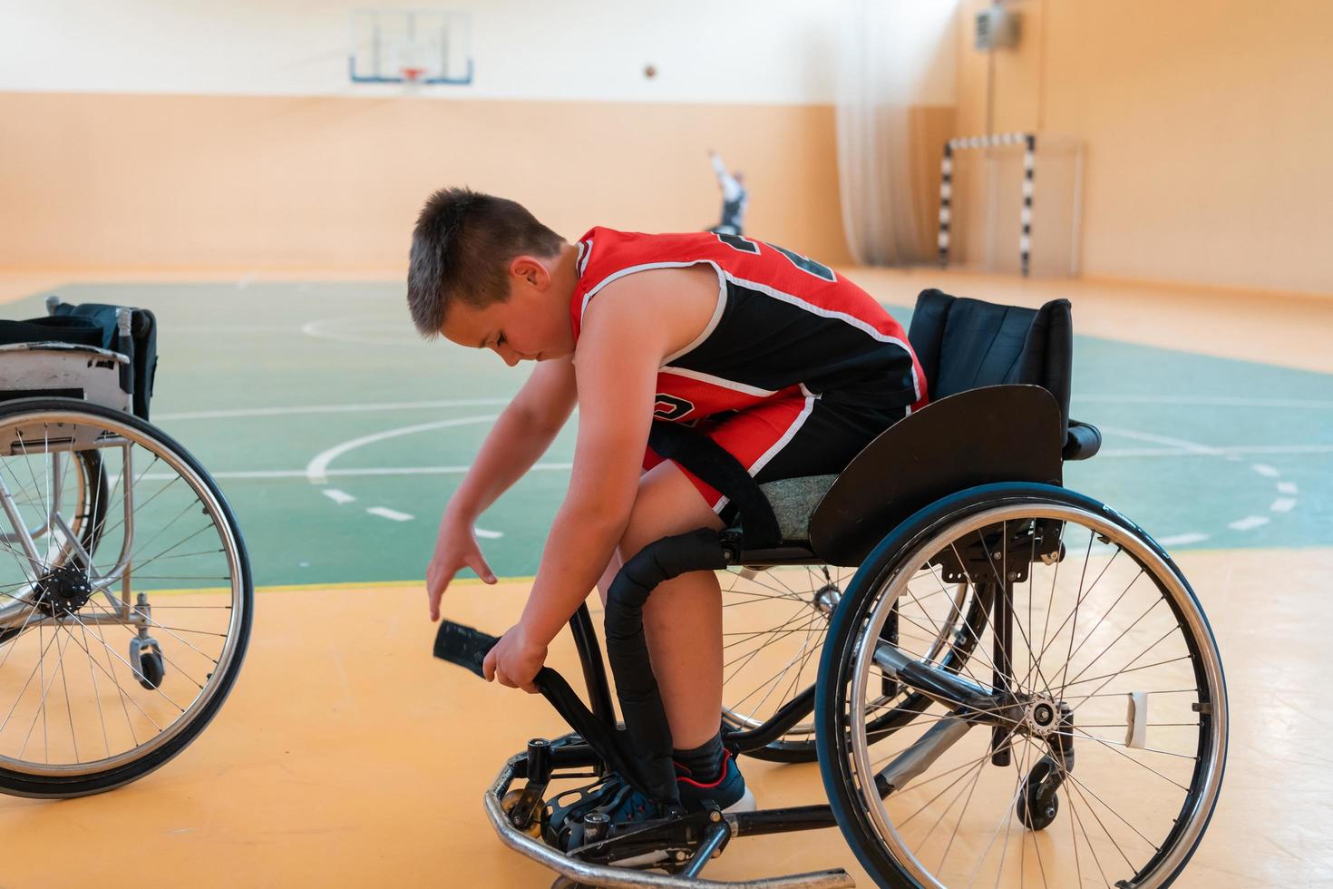 il ragazzo si siede nel un' sedia a rotelle e prepara per il pallacanestro inizio di il gioco nel il grande arena foto