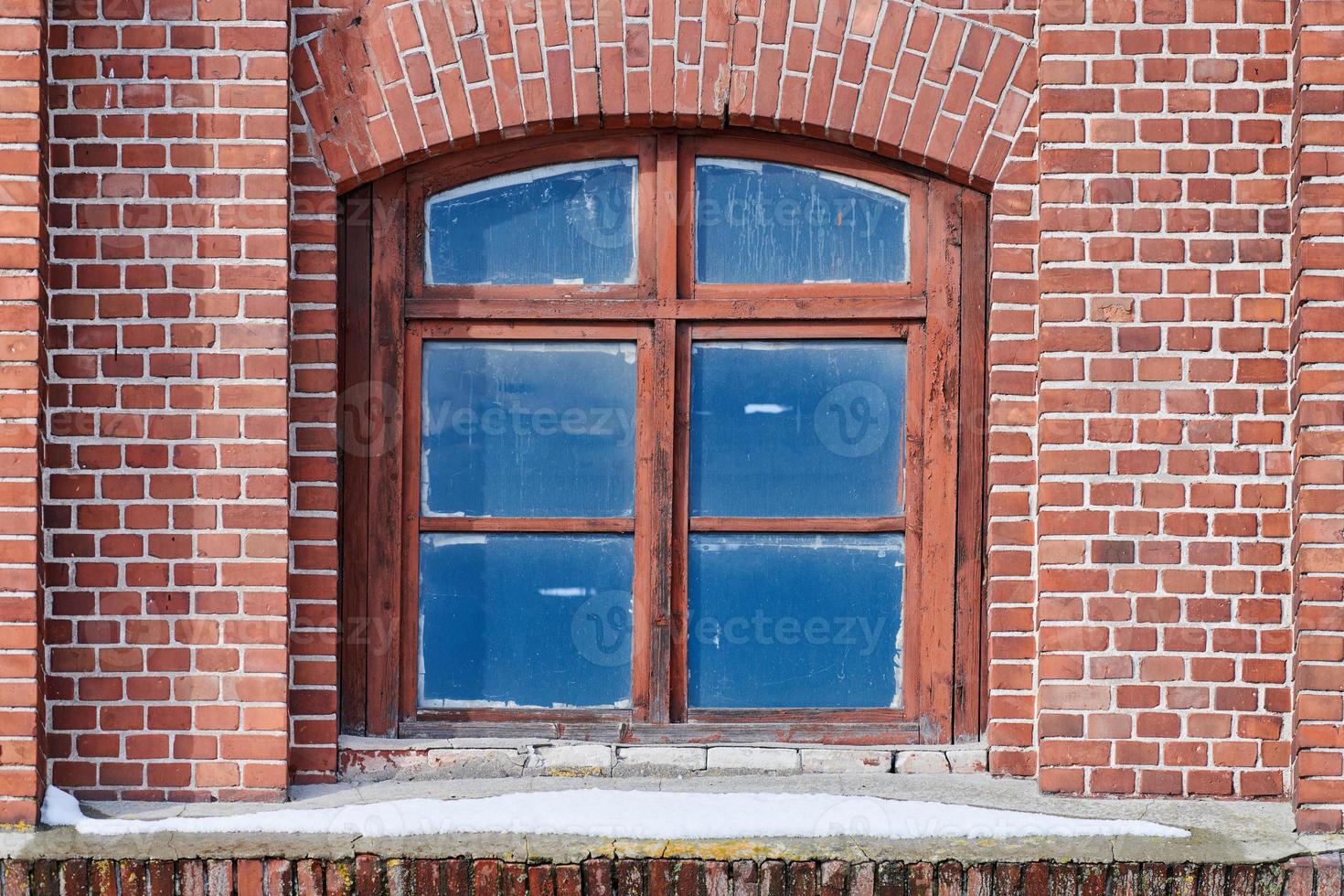 una finestra di vetro ad arco sul vecchio muro di mattoni rossi foto