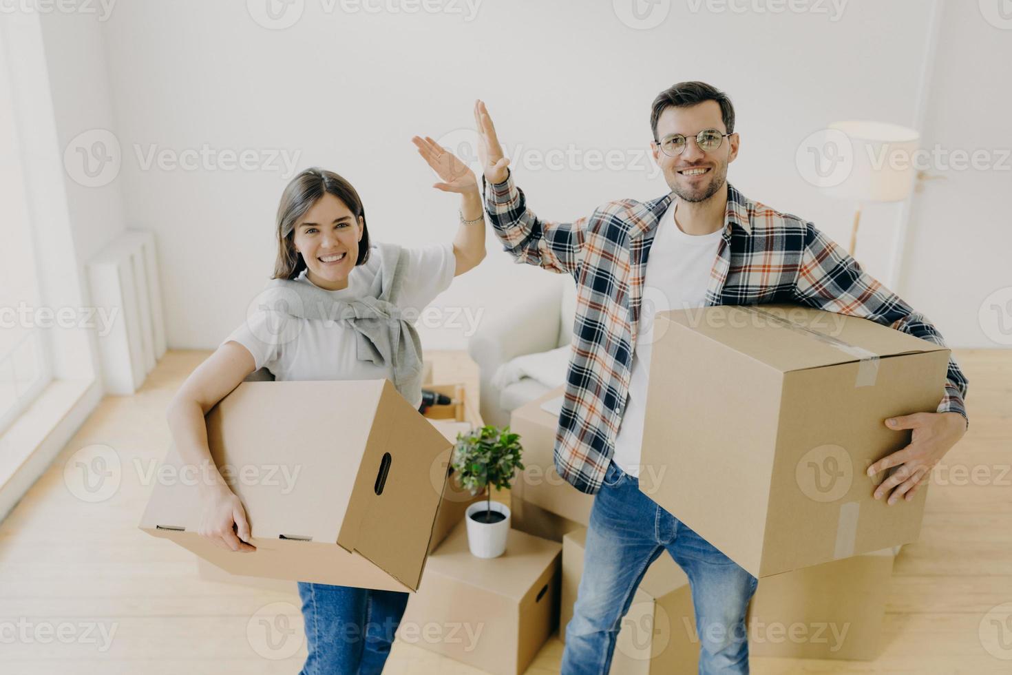 foto di una giovane donna e un uomo allegri danno il cinque, sorridono piacevolmente alla telecamera, vestiti con abiti casual, iniziano una nuova vita, stanno in una spaziosa camera da letto luminosa. persone, concetto di riparazione e spostamento