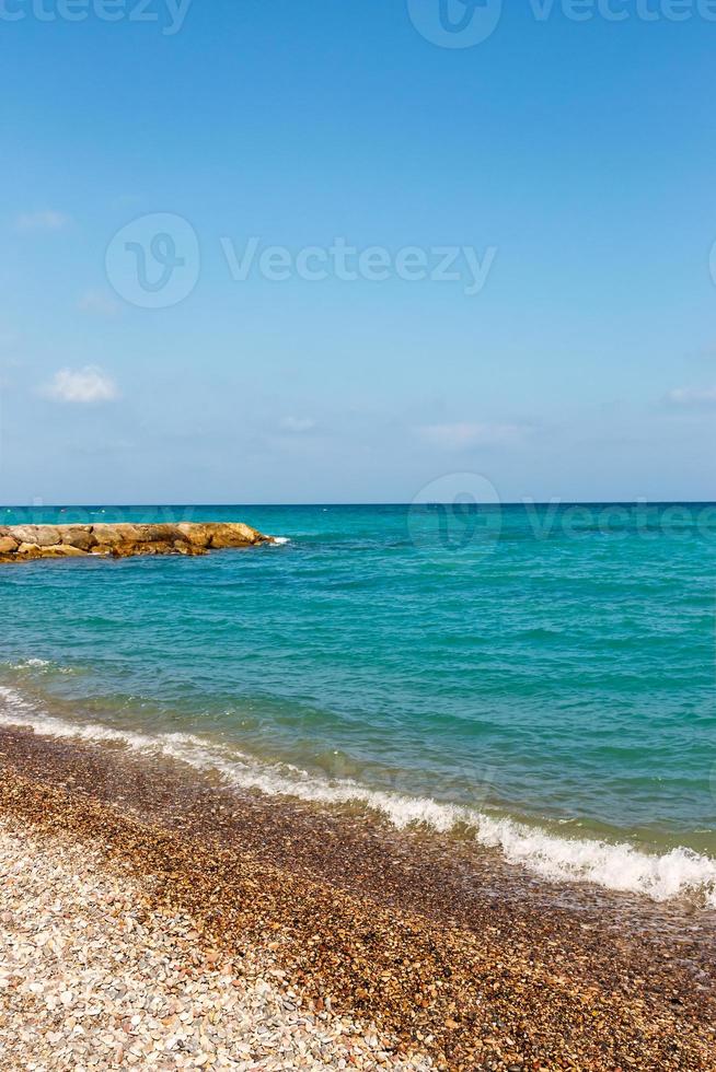 riva di il spiaggia con pietre e molo nel il sfondo. verticale Immagine. foto