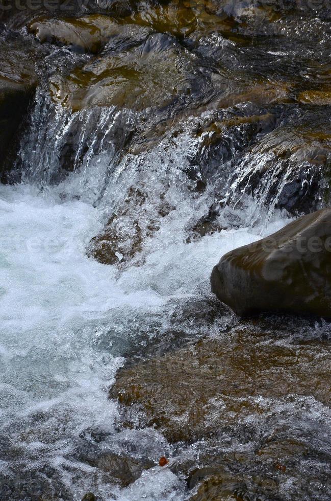 avvicinamento Immagine di un' piccolo selvaggio cascata nel il modulo di corto flussi di acqua fra montagna pietre foto