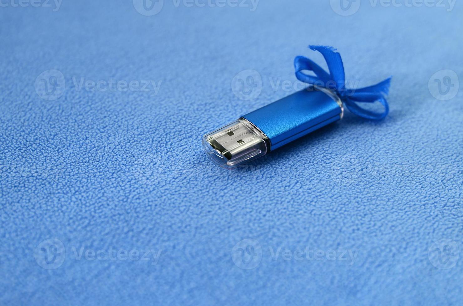 brillante blu USB veloce memoria carta con un' blu arco bugie su un' coperta di morbido e peloso leggero blu vello tessuto. classico femmina regalo design per un' memoria carta foto