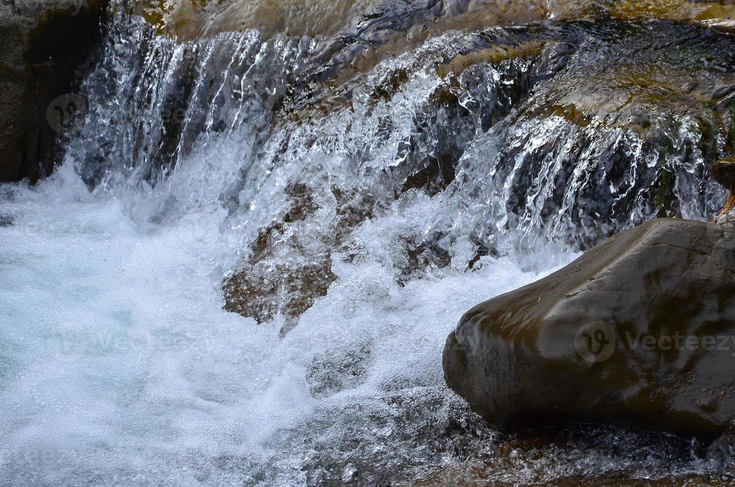 avvicinamento Immagine di un' piccolo selvaggio cascata nel il modulo di corto flussi di acqua fra montagna pietre foto