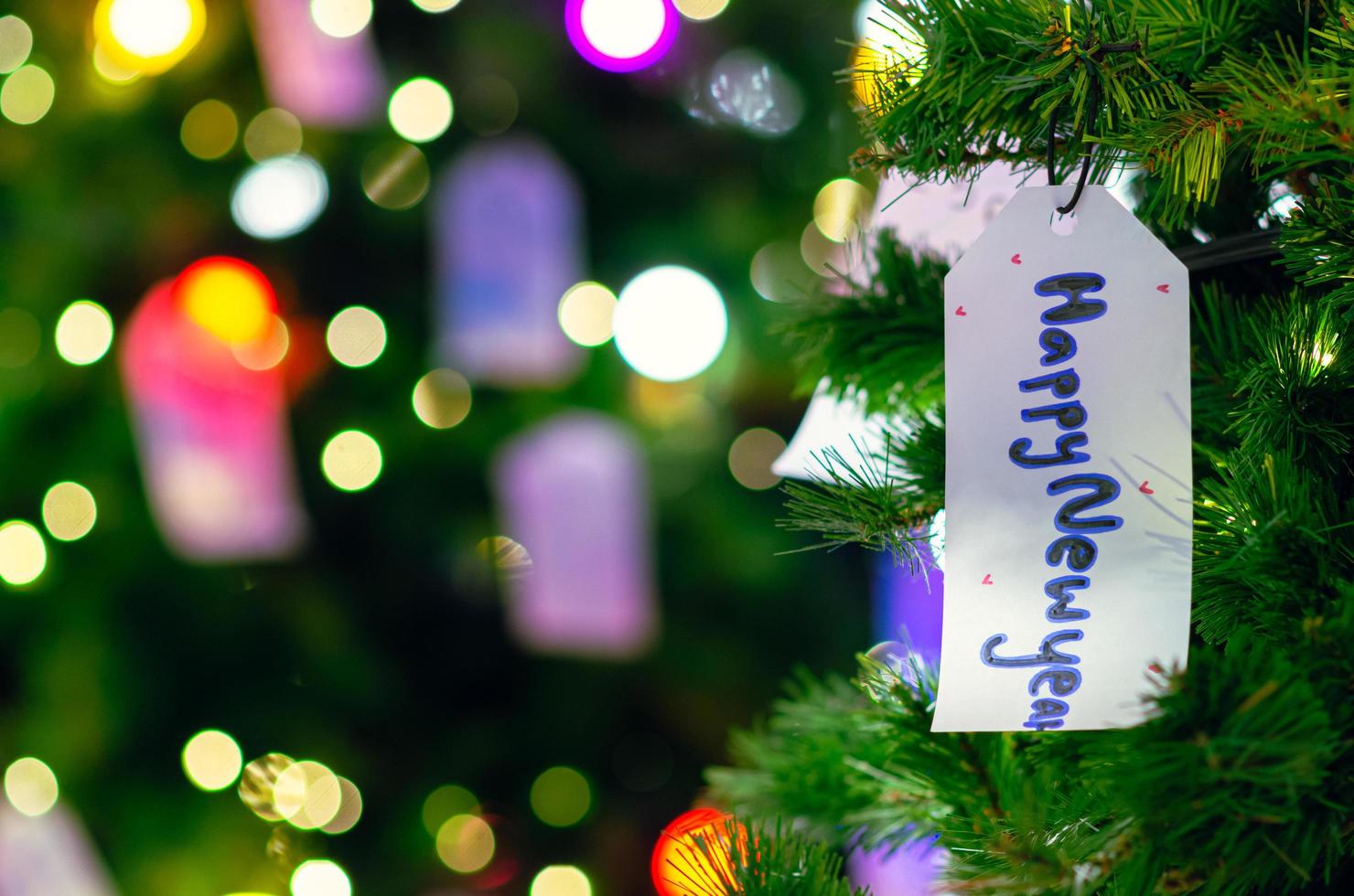 carta sospeso su Natale albero per vacanza decorazione con colorato luci su sfondo. foto