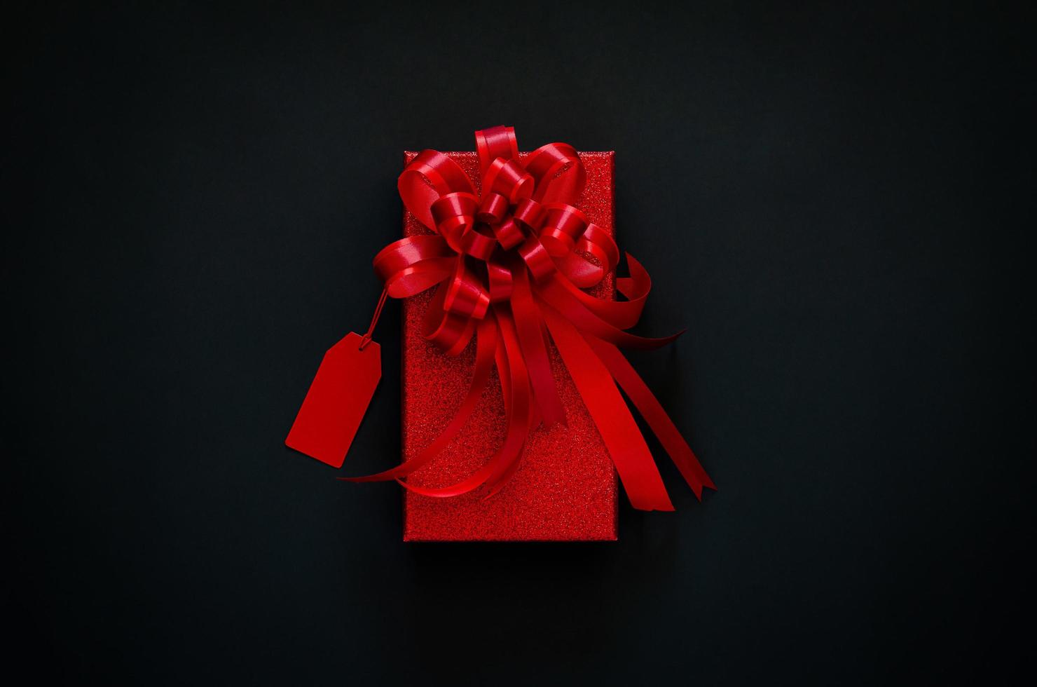 rosso Natale scatola con rosso arco nastro e prezzo etichetta su nero sfondo. nero Venerdì concetto. foto