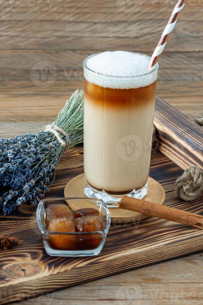 latte macchiato o cappuccino con latte schiuma e lavanda nel un' alto bicchiere su di legno vassoio foto