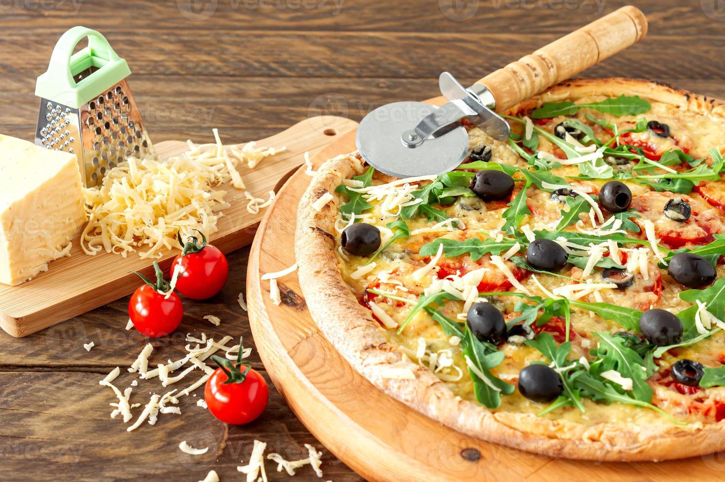 cucinato caldo Pizza torta con peperoni, pomodori, nero olive, rucola e Mozzarella su di legno tavola. foto