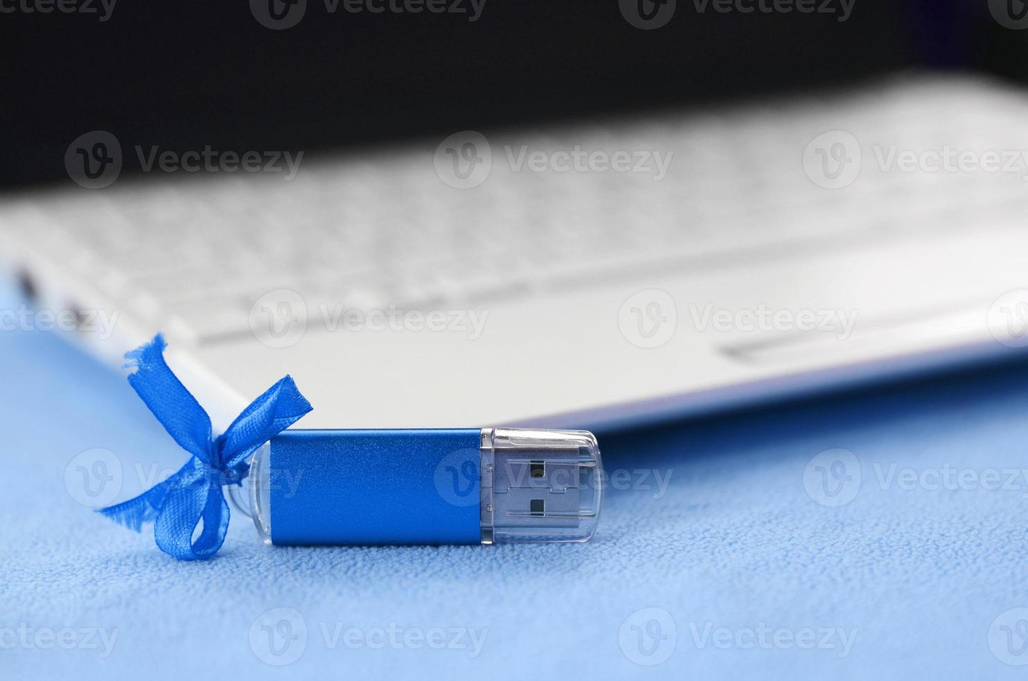 brillante blu USB veloce memoria carta con un' blu arco bugie su un' coperta di morbido e peloso leggero blu vello tessuto accanto per un' bianca il computer portatile. classico femmina regalo design per un' memoria carta foto