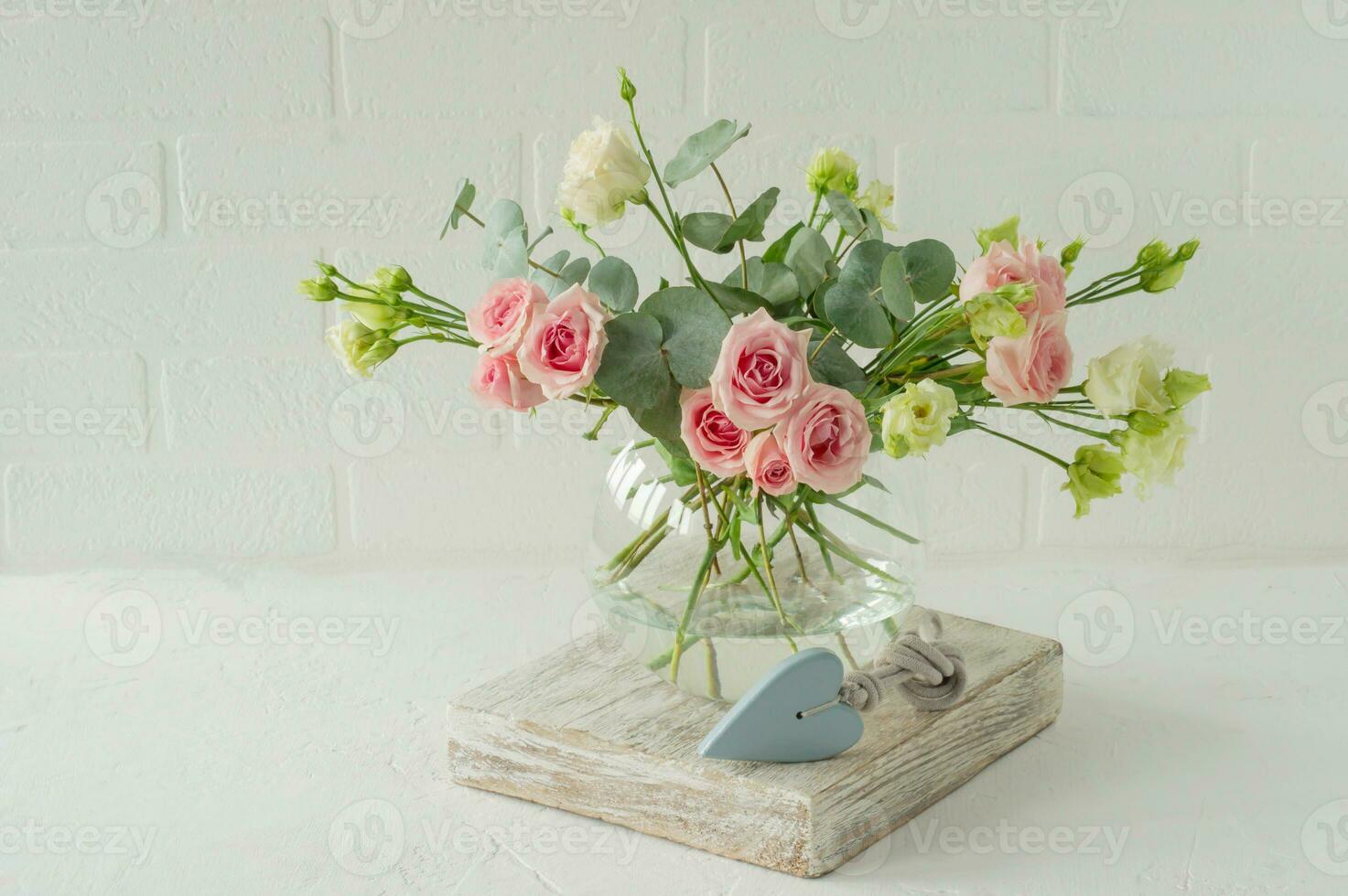 mazzo di Rose, eustoma e eucalipto nel un' bicchiere elegante vaso su un' tavolo. fiori composizione per interno decorazione. foto