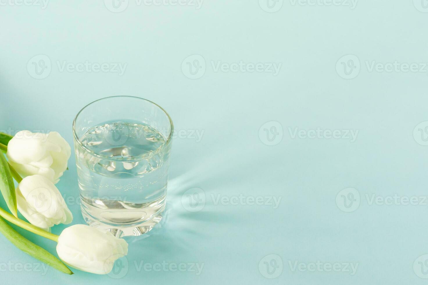 un' bicchiere di puro acqua con tulipani su blu sfondo. copia spazio per testo. consept di Salute vita e dieta foto