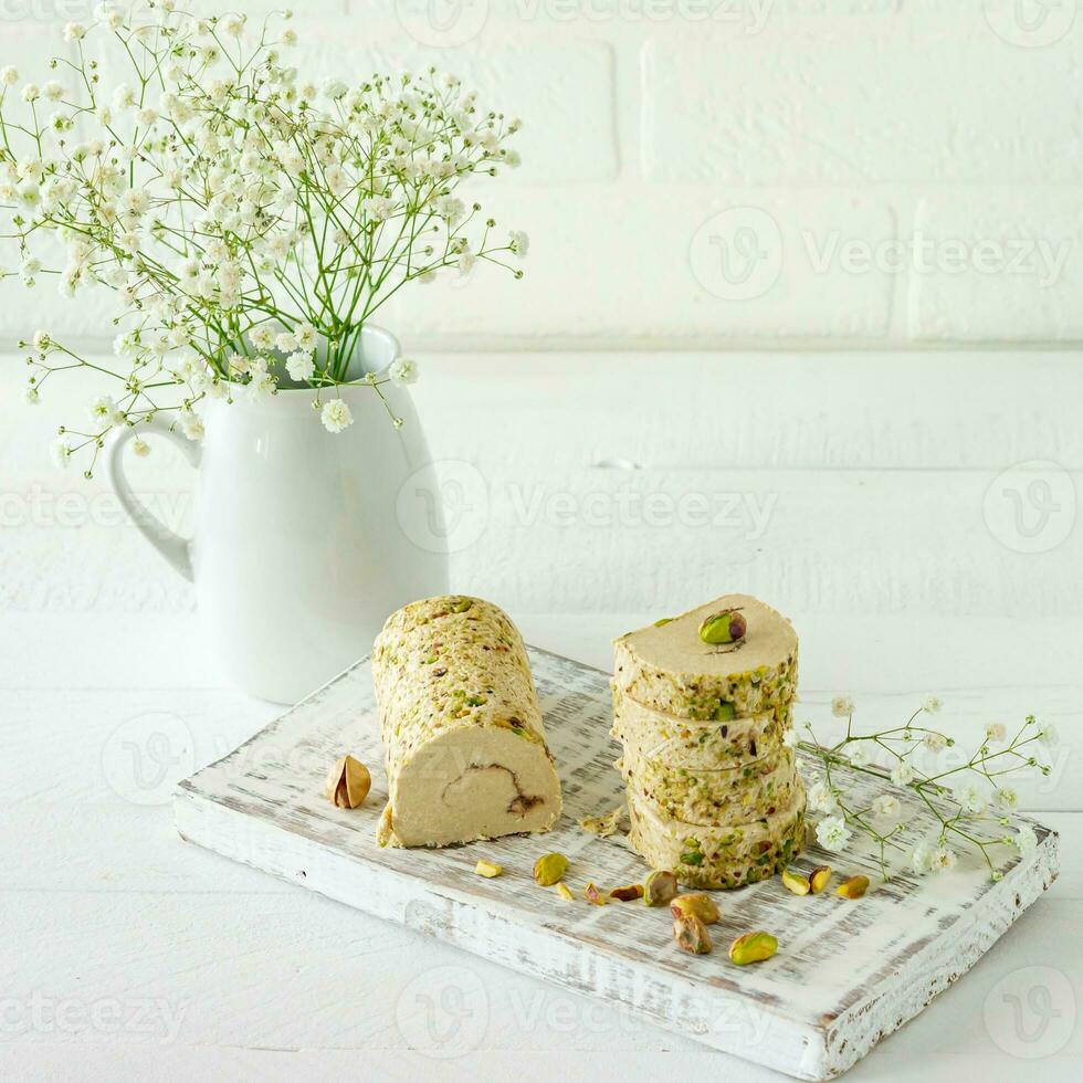 Halva con pistacchio servito su bianca di legno scrivania con fiori foto