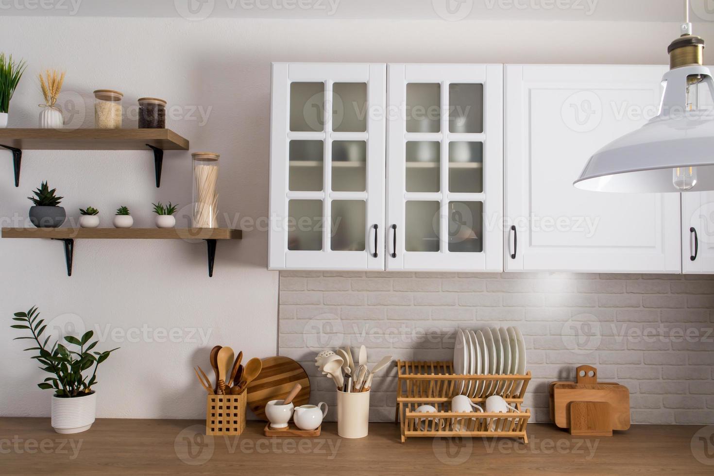 parte di il interno di un' bianca moderno cucina con armadietti con smerigliato bicchiere, un' mattone bianca parete e un' di legno controsoffitto. cucina attrezzatura. foto