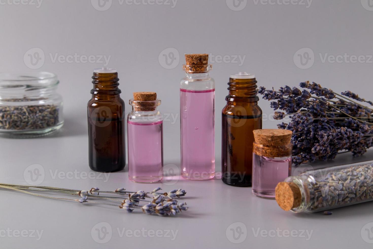 un' impostato di cosmetico prodotti con un estratto di lavanda fiori nel vario bicchiere bottiglie per naturale cura di sé. grigio sfondo. foto