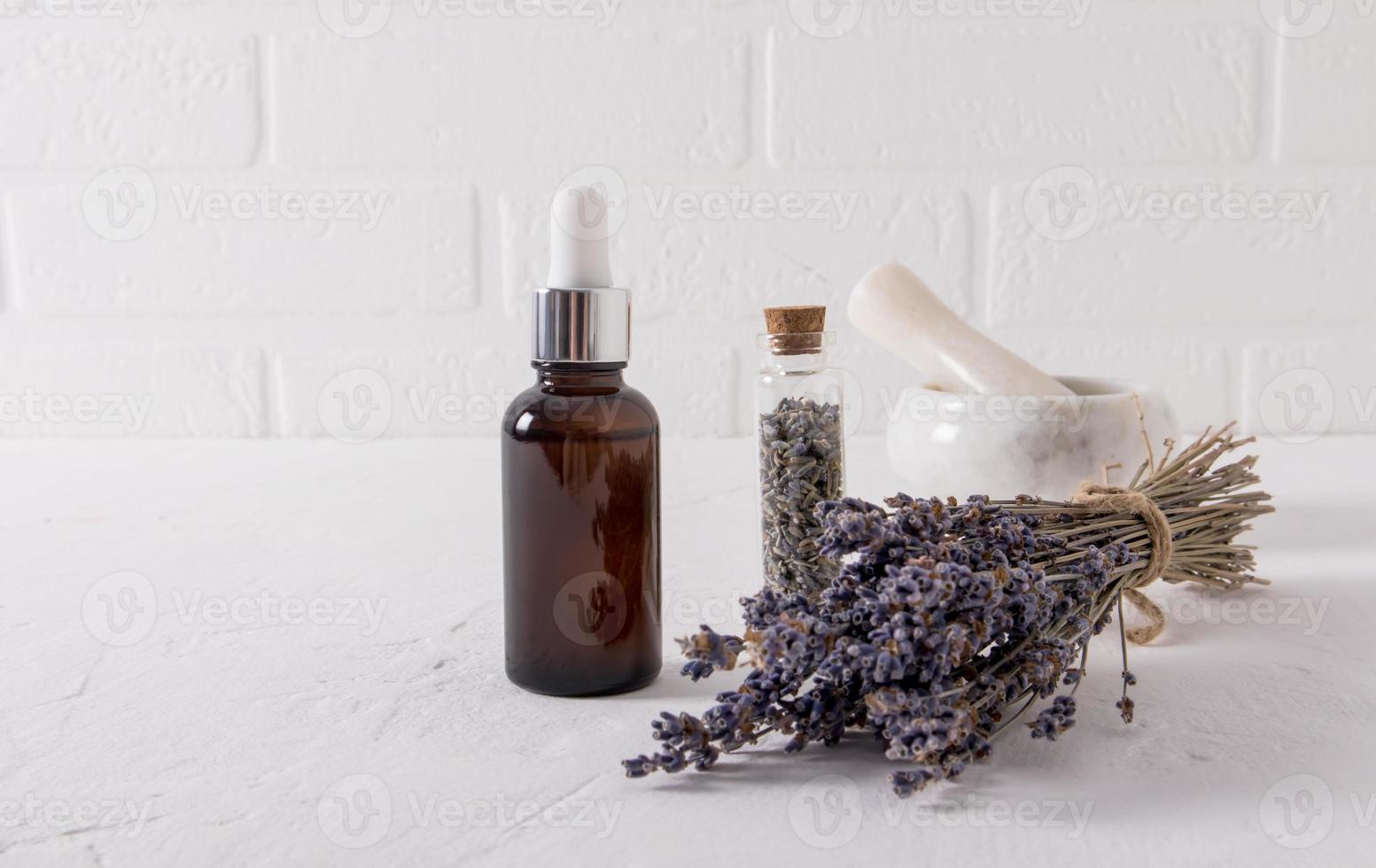 siero con un estratto di lavanda erbe aromatiche per viso e corpo pelle cura nel un' bottiglia di vetro su un' bianca tavolo e il mattone parete. foto