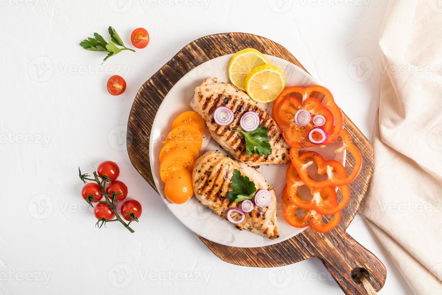 un' bianca ceramica piatto in piedi su un' di legno tavola con grigliato pollo filetto, fresco tritato verdure. superiore Visualizza. bianca sfondo. foto