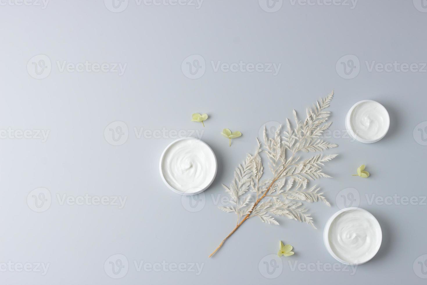 barattoli di cosmetico crema con fiori su grigio sfondo. piatto posizione, copia spazio foto