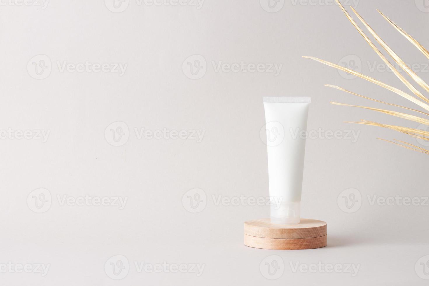 bianca tubo di cosmetico crema con legna podio e palma foglia su grigio sfondo. vicino su, copia spazio foto