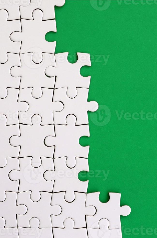 frammento di un' piegato bianca sega puzzle su il sfondo di un' verde plastica superficie. struttura foto con copia spazio per testo