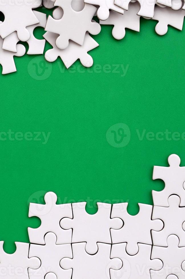 frammento di un' piegato bianca sega puzzle e un' mucchio di spettinato puzzle elementi contro il sfondo di un' verde superficie. struttura foto con spazio per testo