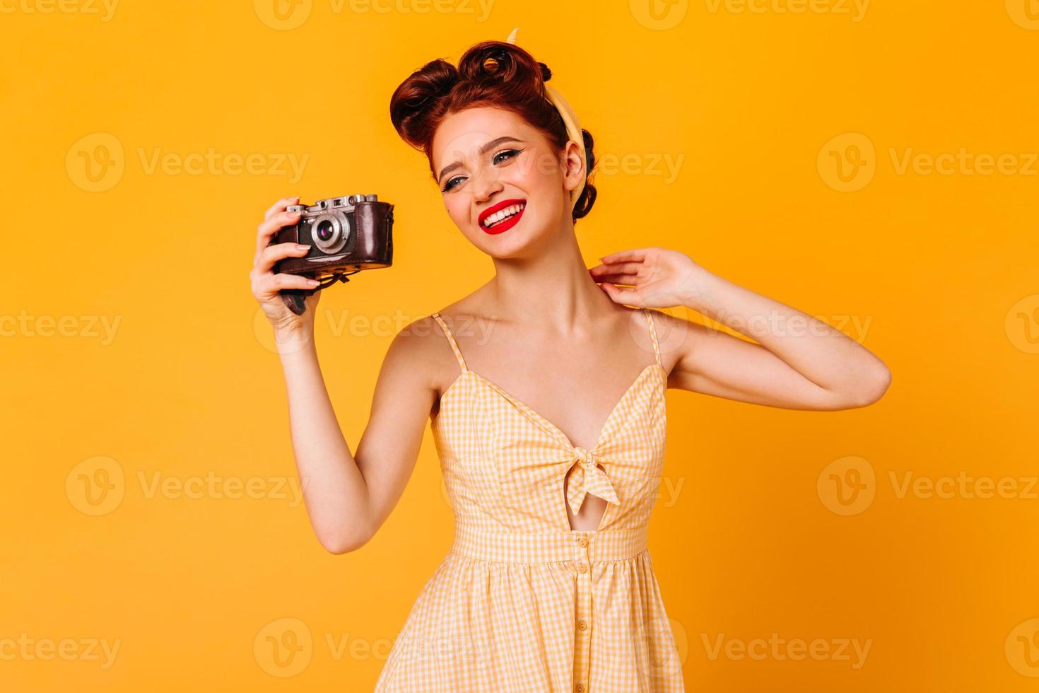 gioioso ragazza copertina ragazza nel vestito assunzione fotografie. studio tiro di elegante ridendo donna con telecamera isolato foto