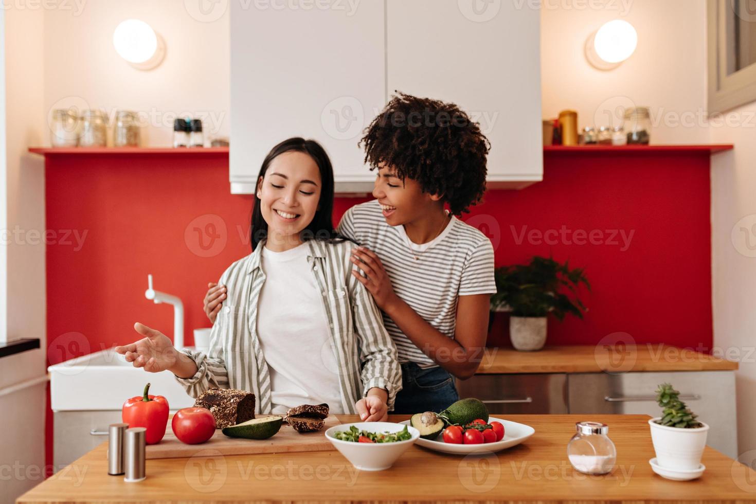 bella donne con gioia comunicare. ragazze nel bianca cime cucinare cibo a partire dal verdure. foto