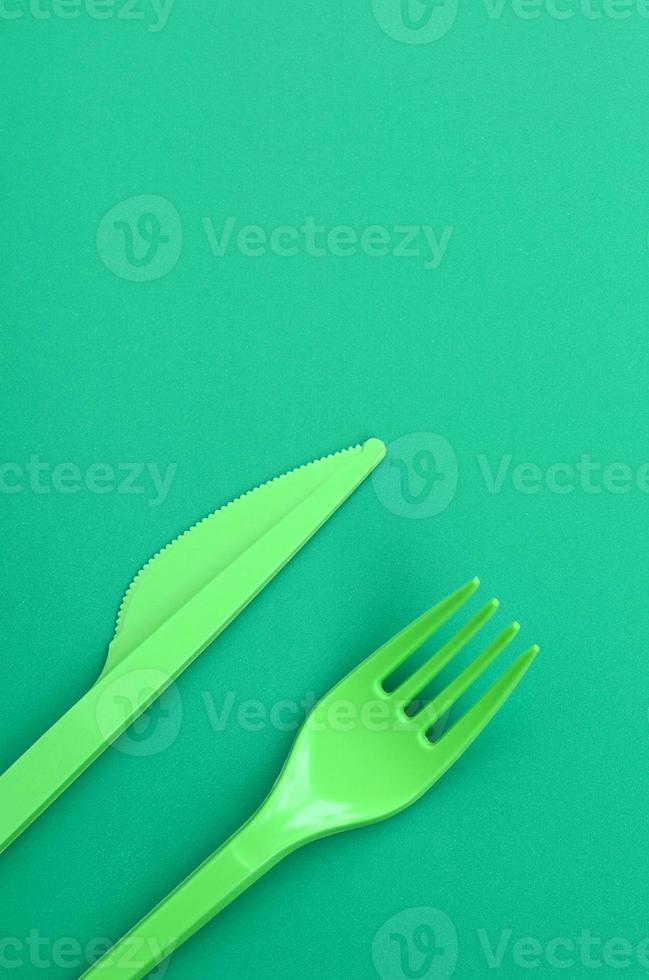 monouso plastica posate verde. plastica forchetta e coltello menzogna su un' verde sfondo superficie foto