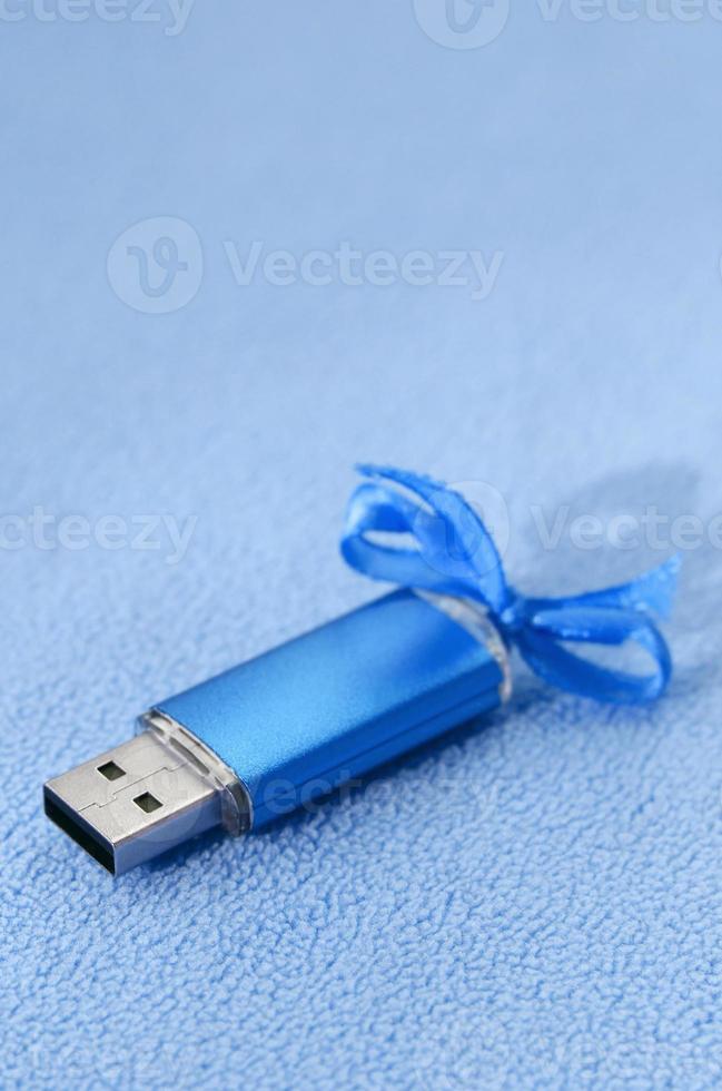 brillante blu USB veloce memoria carta con un' blu arco bugie su un' coperta di morbido e peloso leggero blu vello tessuto. classico femmina regalo design per un' memoria carta foto