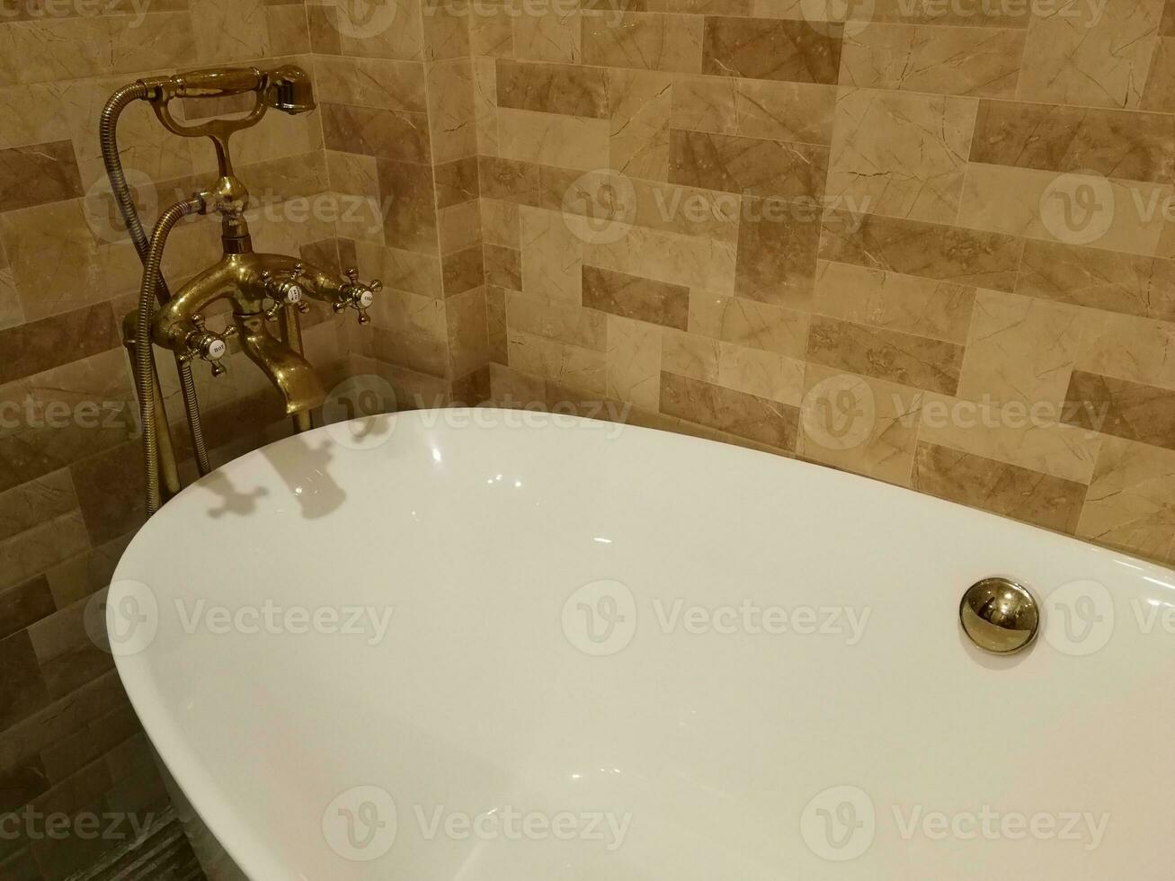 bianca vasca da bagno con d'oro rubinetto, sfondo è Marrone mattone. foto