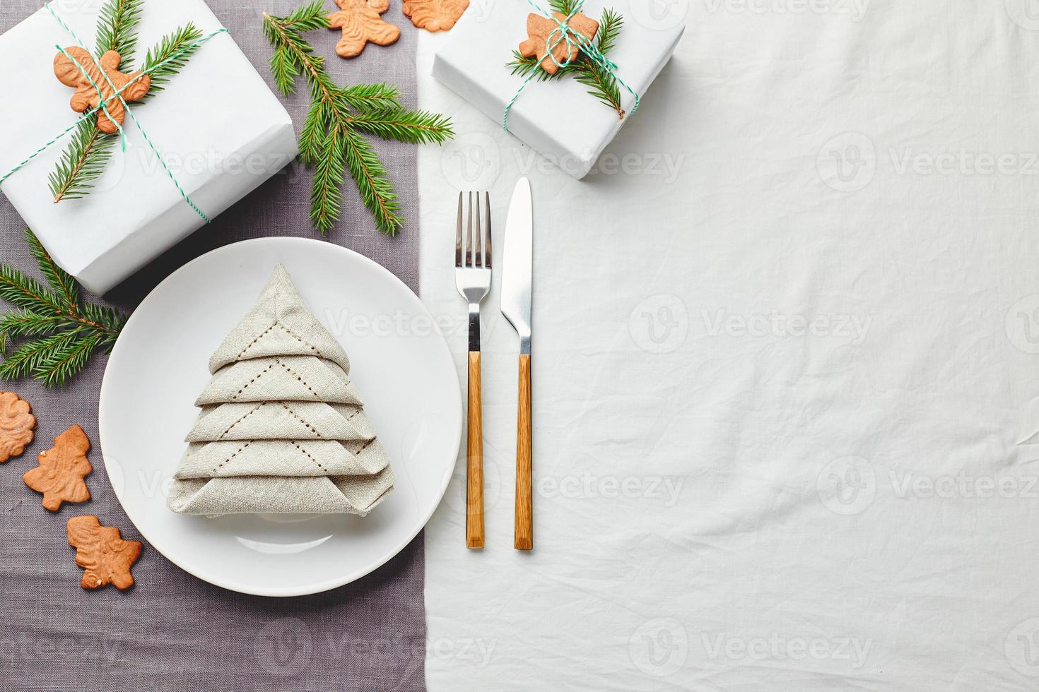 tovagliolo nel il modulo di un' Natale albero su un' piatto su bianca tovaglia con i regali e decorazioni con abete rametti e Pan di zenzero biscotti foto