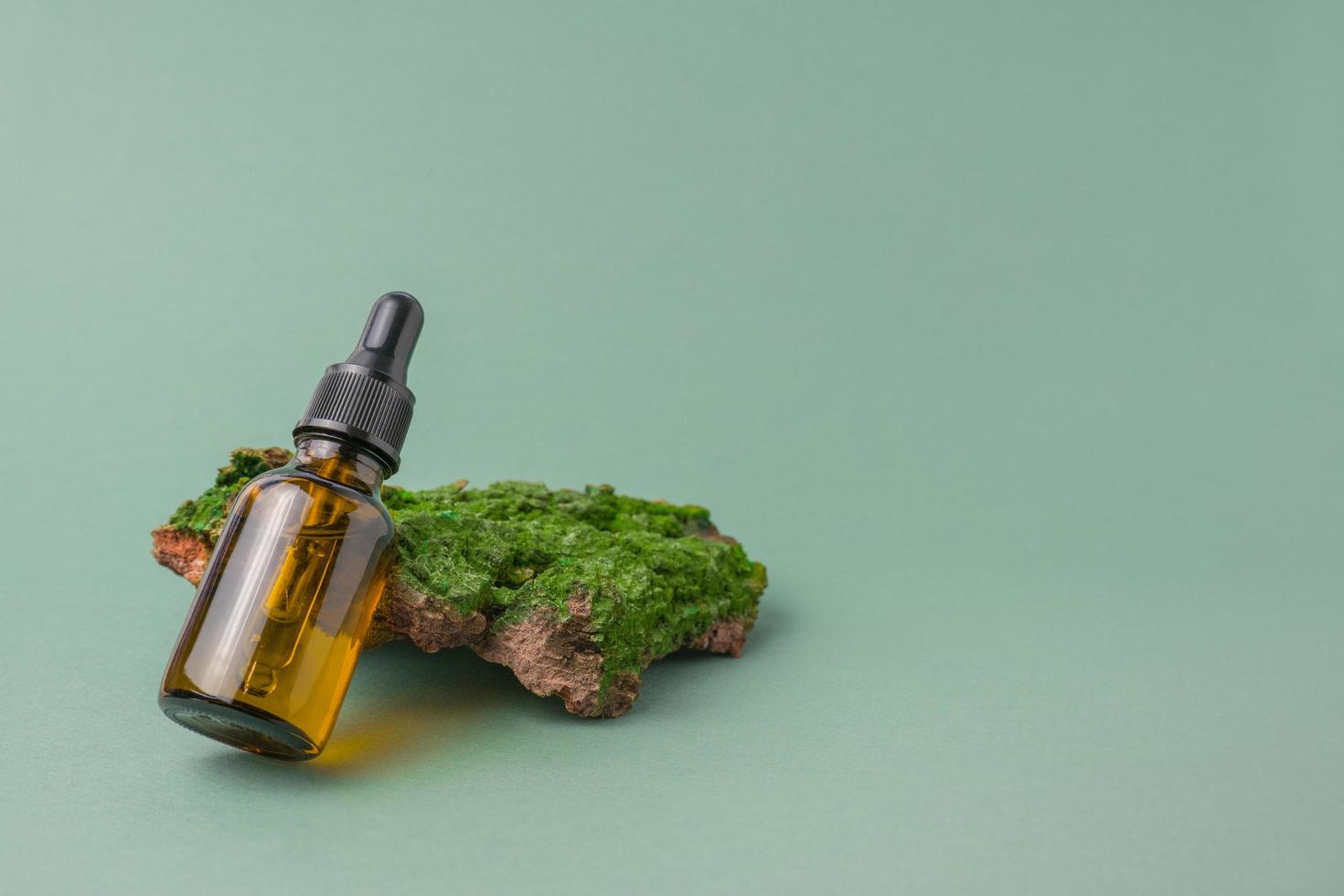 naturale pelle cura. l'ambiente amichevole cosmetici. Marrone bicchiere vaso con facciale siero su il abbaiare di un' albero con verde muschio su un' verde sfondo. copia spazio foto