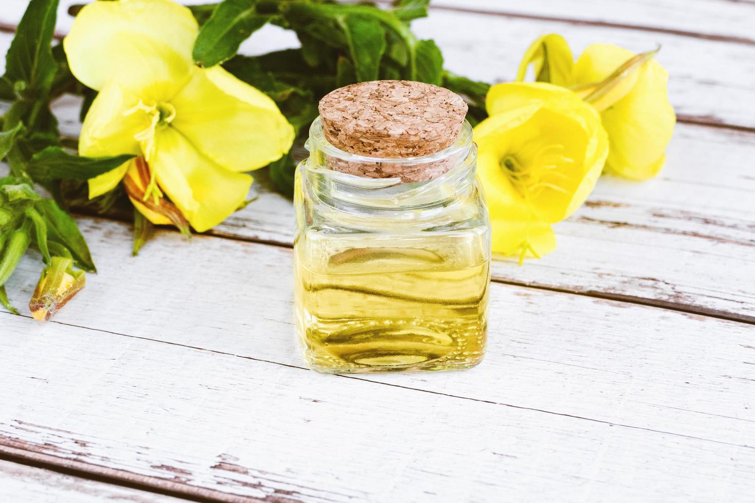 essenziale olio di sera primula nel bicchiere bottiglia, giallo fiori su bianca tavolo, alternativa medicina foto