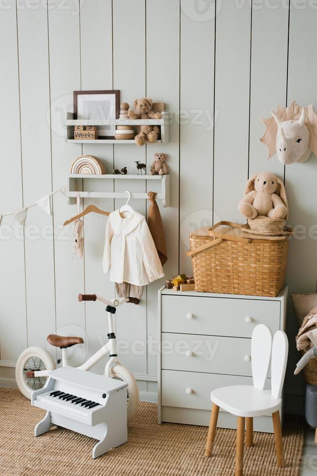 accogliente interno di un' figli di camera, un' giocare la zona. giocattoli, un' bicicletta, un' pianoforte, un' il petto di cassetti e Abiti su un' appendiabiti. scandinavo appartamento stile foto