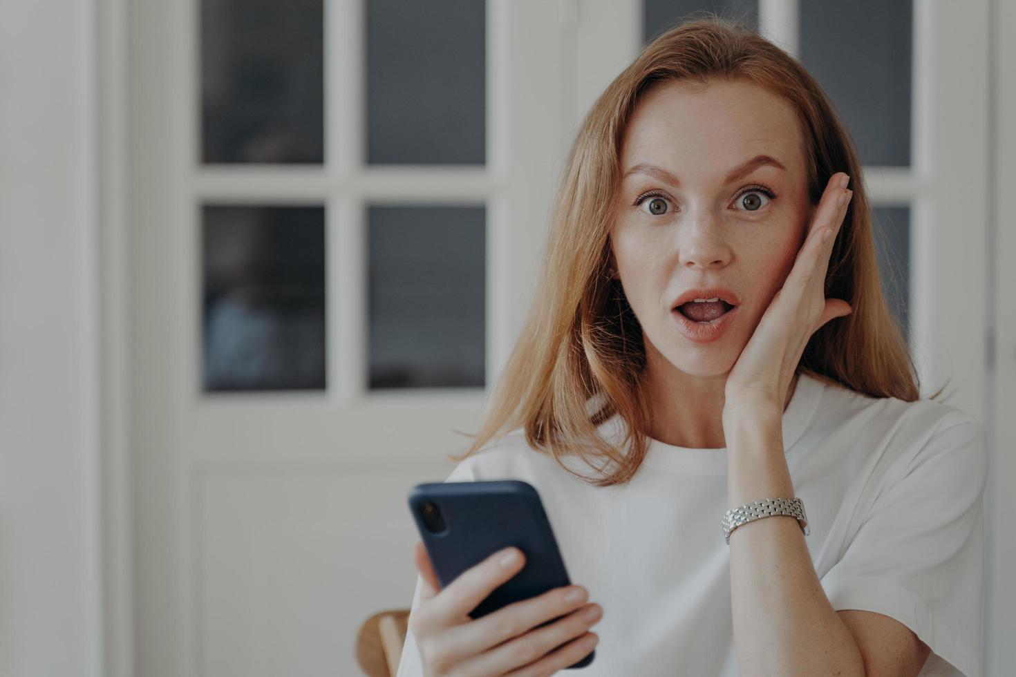 donna è un eccitato Tenere Telefono. testa Rossa europeo signora prende shock, libero professionista ha Scadenza. foto