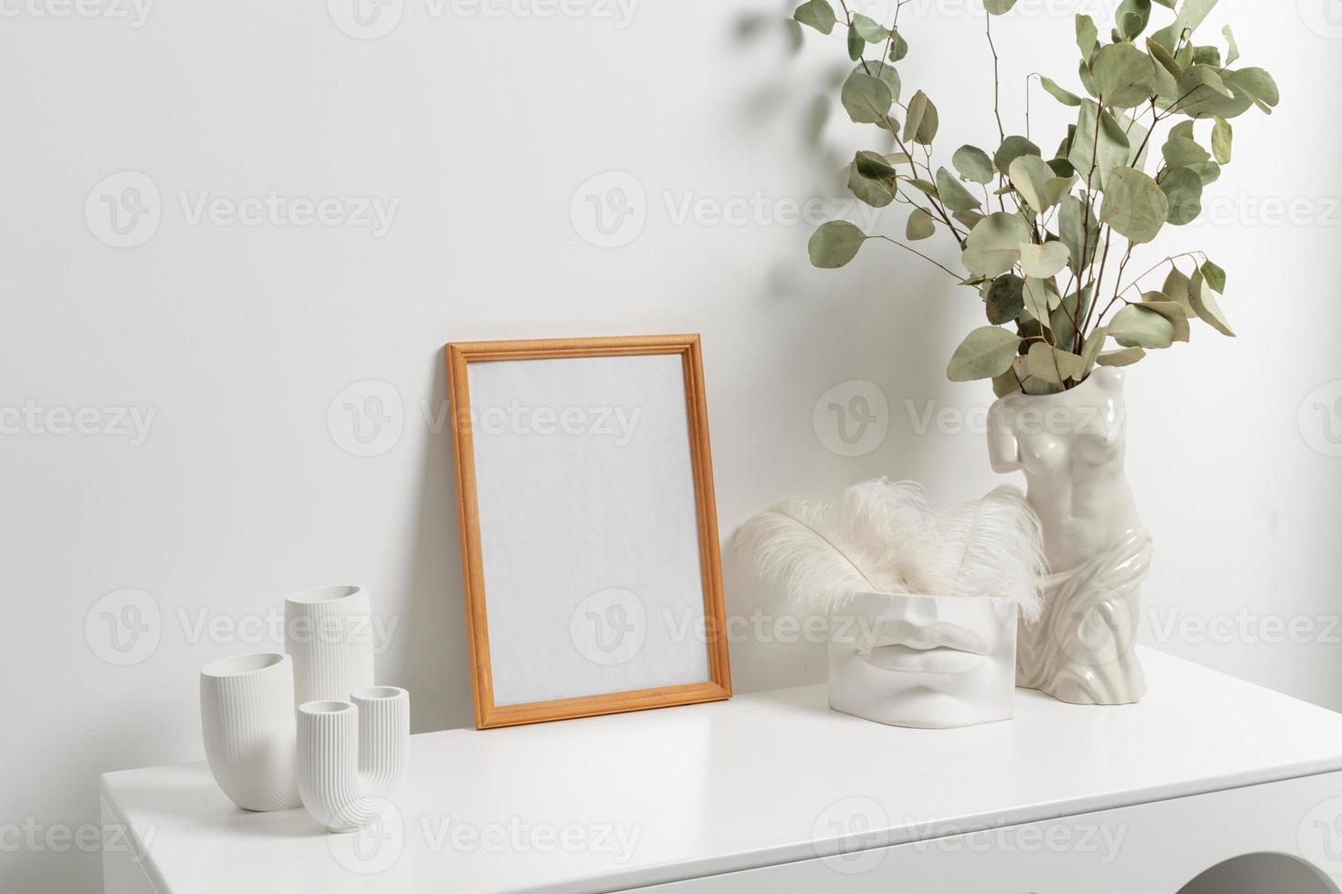 di legno verticale telaio con bianca vaso di eucalipto le foglie al di sopra di bianca parete foto