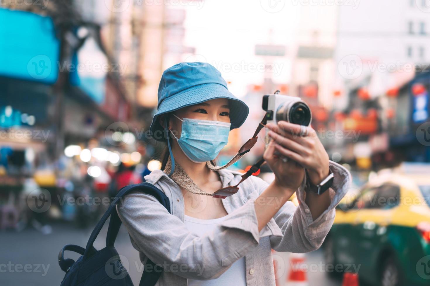 il viaggiatore dello zaino della giovane donna asiatica adulta indossa la maschera per il viso scatta una foto con la fotocamera.