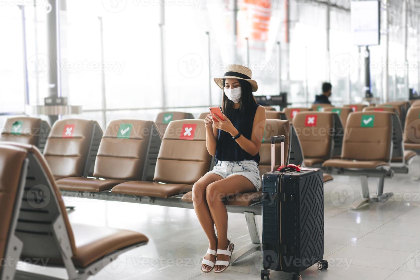 giovane adulto turista donna indossare maschera per virus scoppio a aeroporto terminale con sociale distanziamento sedia. foto