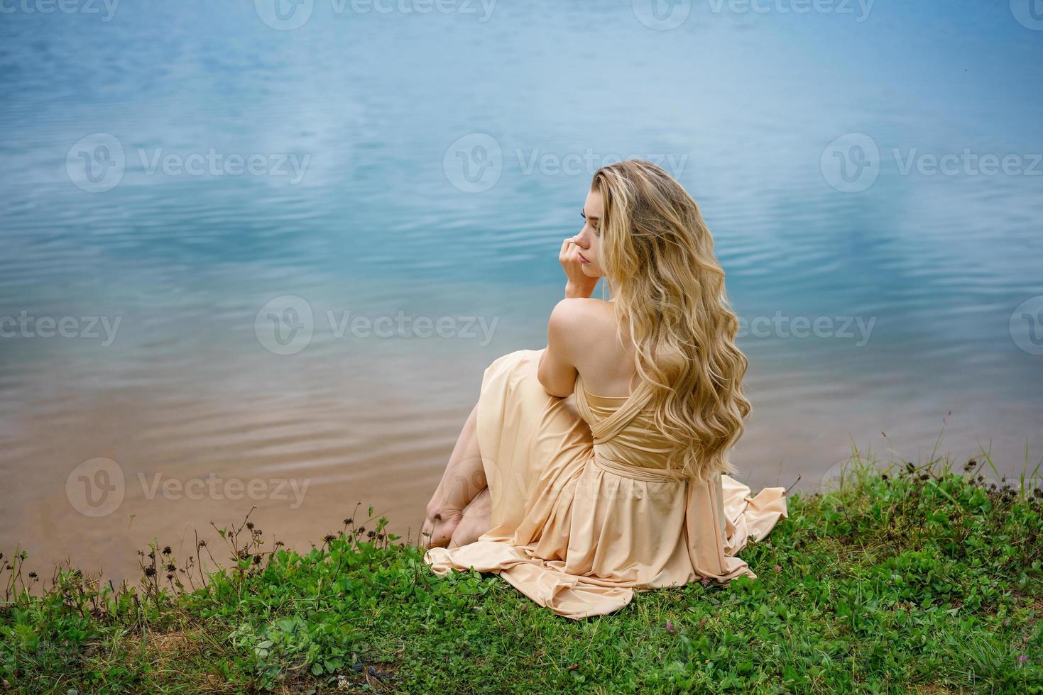 bellissimo triste ragazza seduta su il riva di il lago nel un' vestito , il concetto di solitudine foto