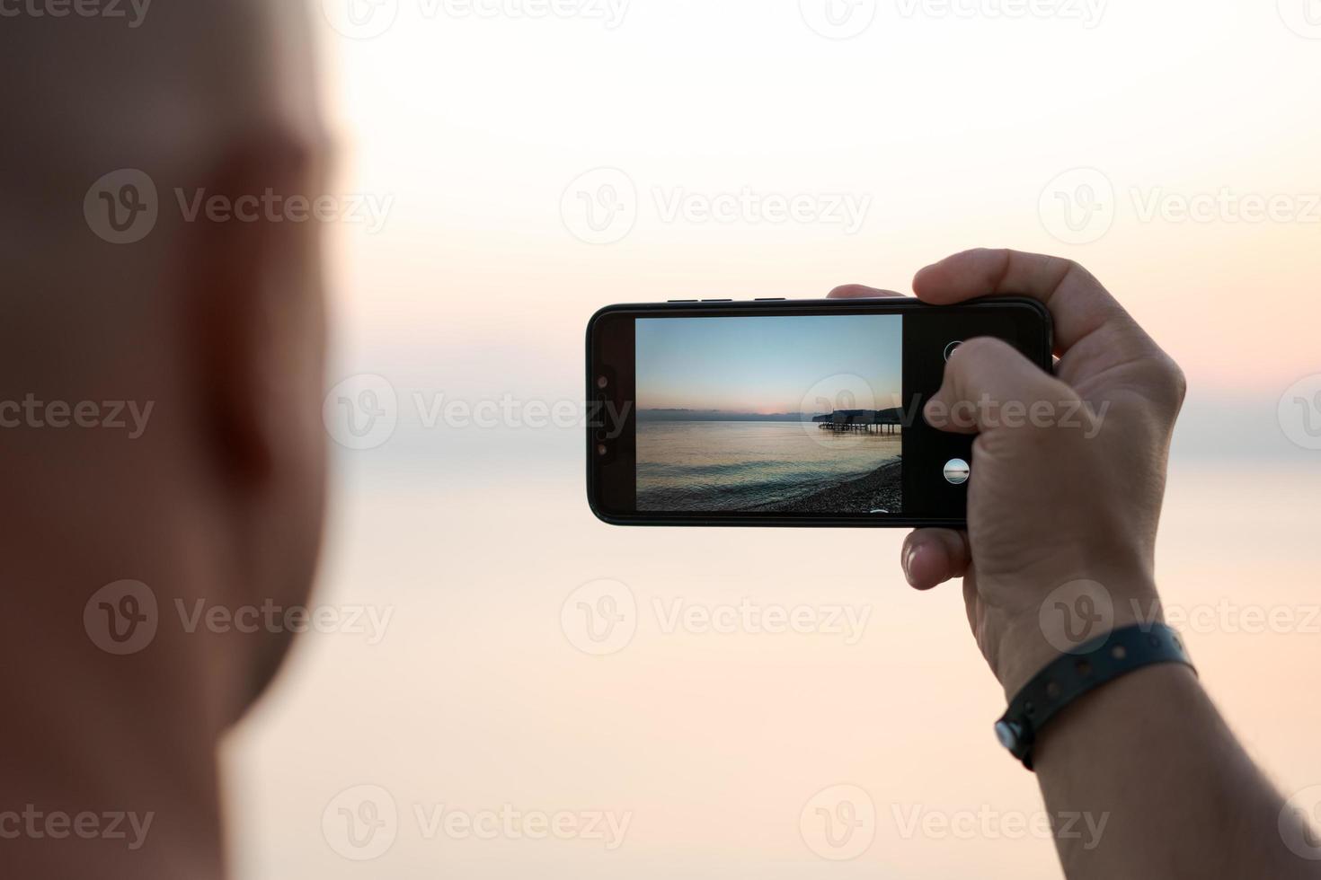 uomo assunzione foto sorprendente tramonto utilizzando smartphone telecamera, turista mano Tenere