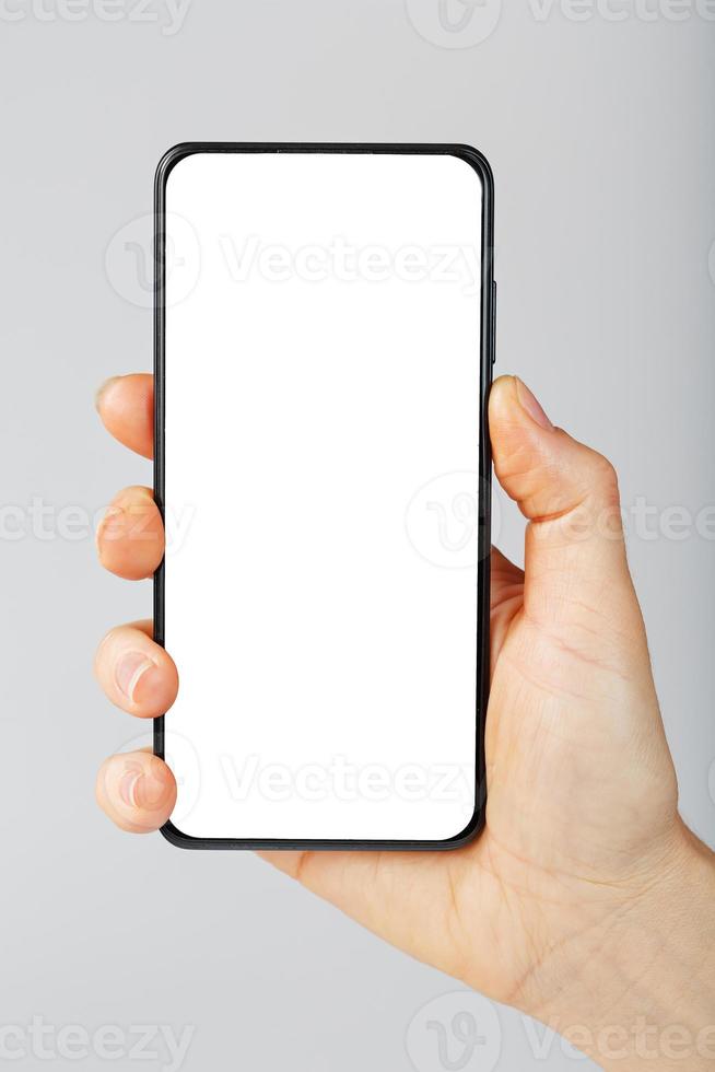 mano detiene nero smartphone con vuoto bianca schermo e moderno frameless design isolato su grigio sfondo. foto