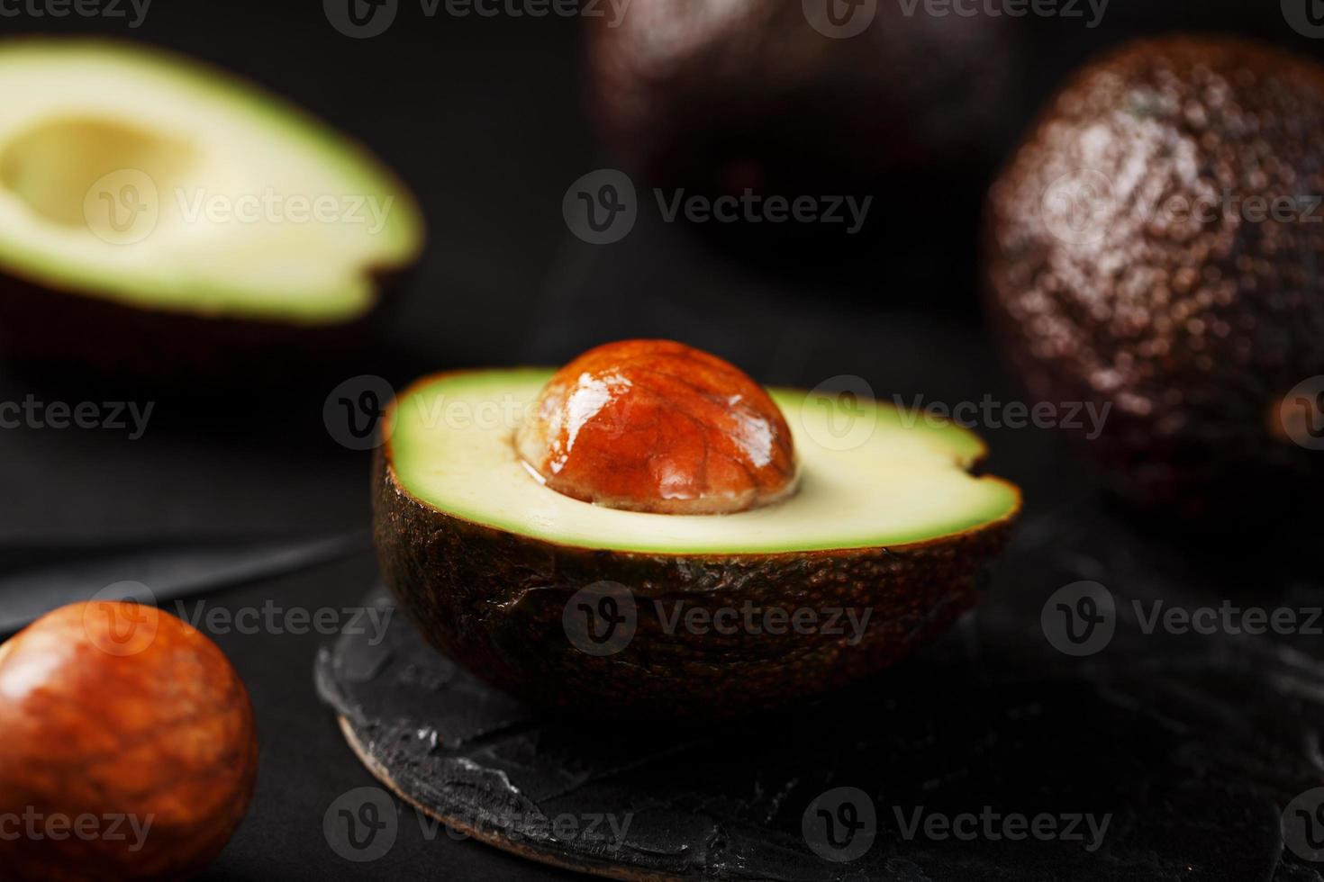 totale e affettato avocado con un' coltello su un' nero strutturato nero tavolo, piatto opere murarie. foto