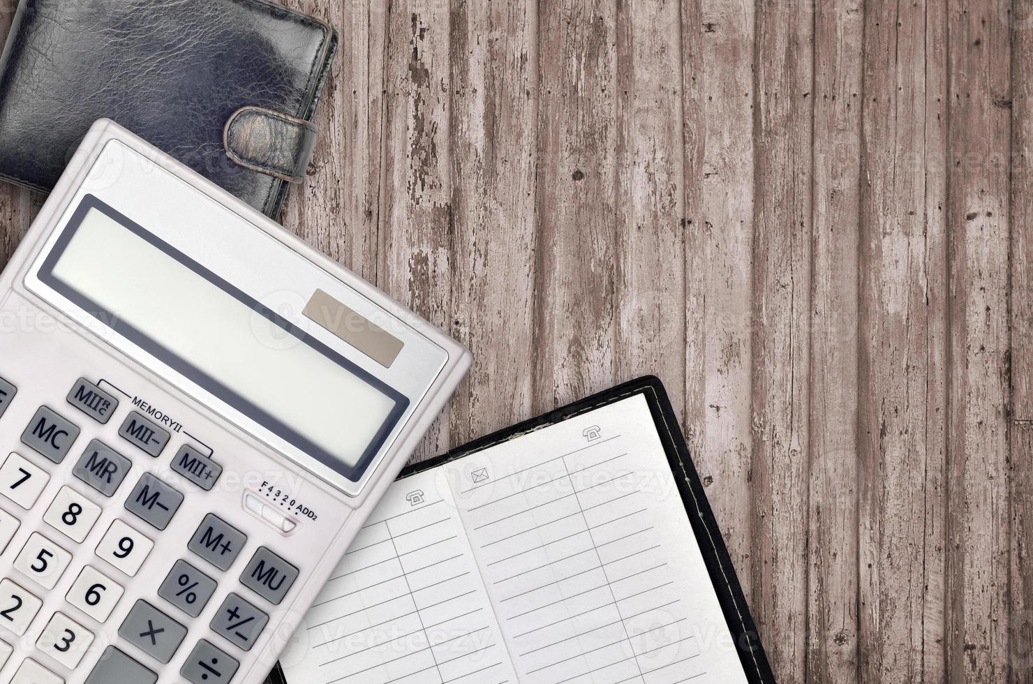 ufficio piatto posare composizione con calcolatrice, indirizzo libro e nero borsa su Marrone di legno tavolo sfondo con superiore Visualizza. contabile lavoro d'ufficio concetto foto