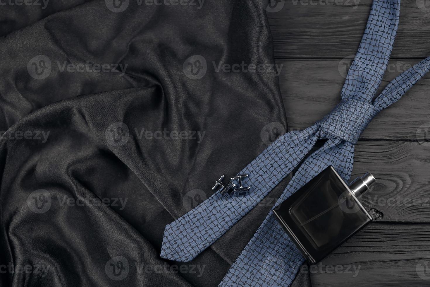 un' bottiglia di Uomini colonia e gemelli con blu cravatta menzogna su un' nero lusso tessuto sfondo su un' di legno tavolo. Uomini Accessori foto