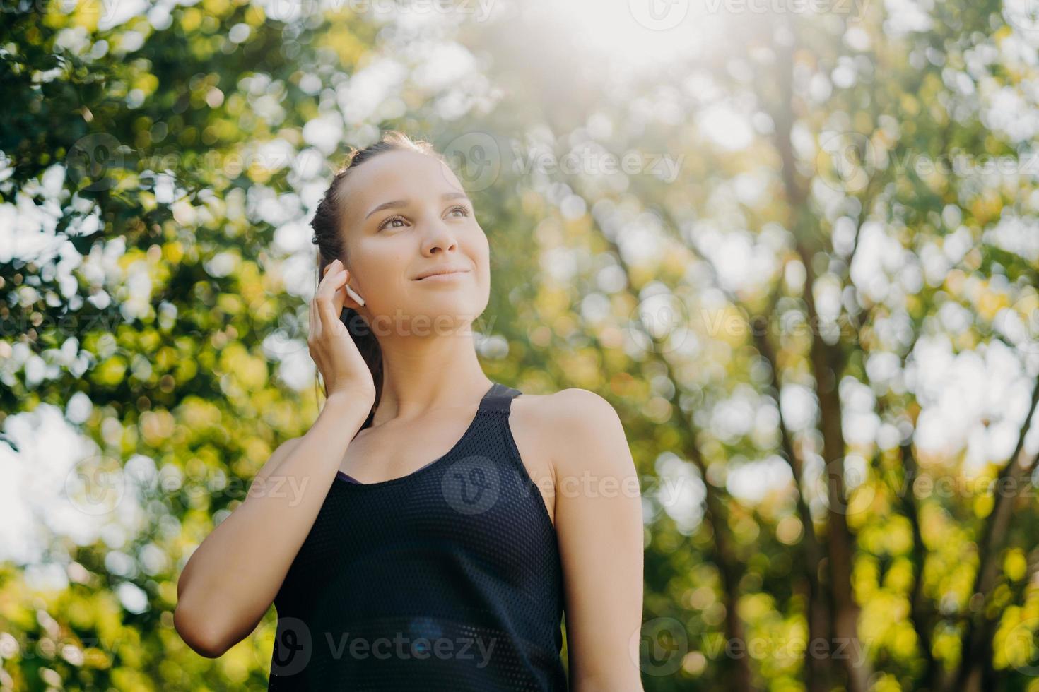 lo scatto all'aperto di una donna atletica soddisfatta focalizzata sulla distanza rimane attiva conduce uno stile di vita sano indossa abiti sportivi pone su uno sfondo sfocato della natura. la giornata di sole è buona per l'allenamento all'aperto foto