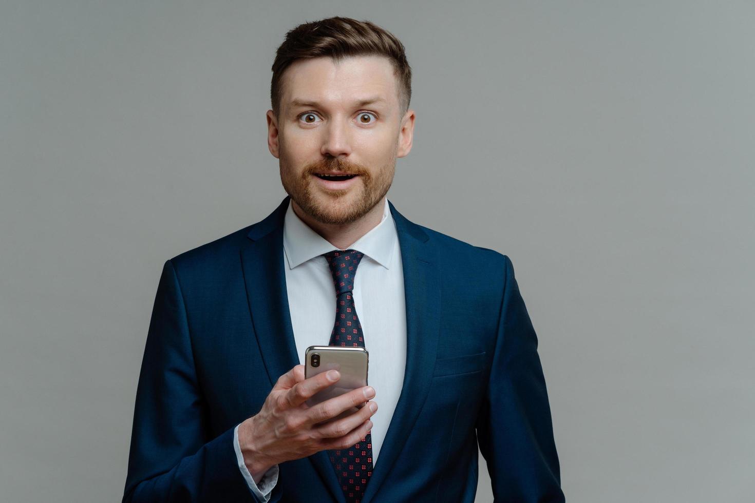 uomo d'affari stupito in giacca e cravatta che legge buone notizie sullo smartphone foto