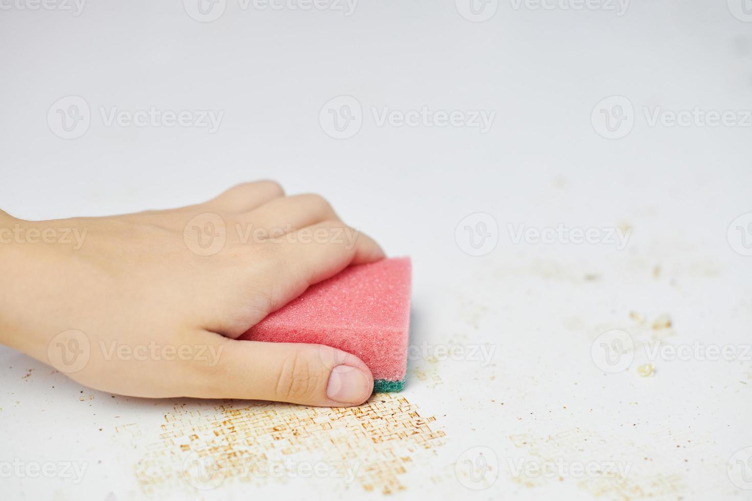 pulire il tavolo della cucina. la spugna rosa in mano della donna rimuove lo sporco, il pangrattato e gli avanzi. faccende domestiche foto