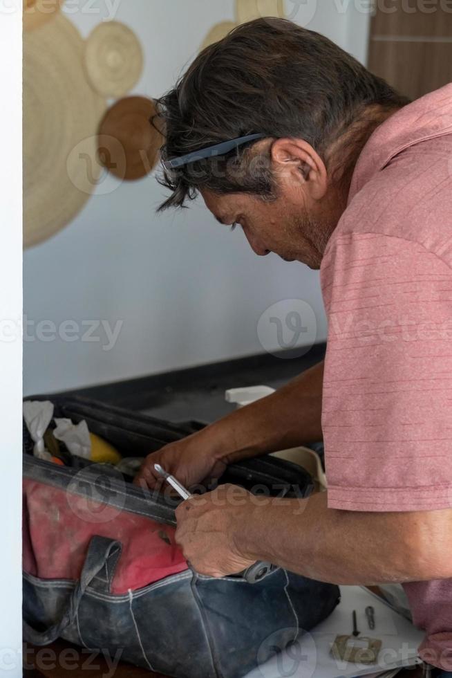 latino uomo guardare per utensili nel il suo cassetta degli attrezzi, ispanico, con Cacciavite nel mano foto