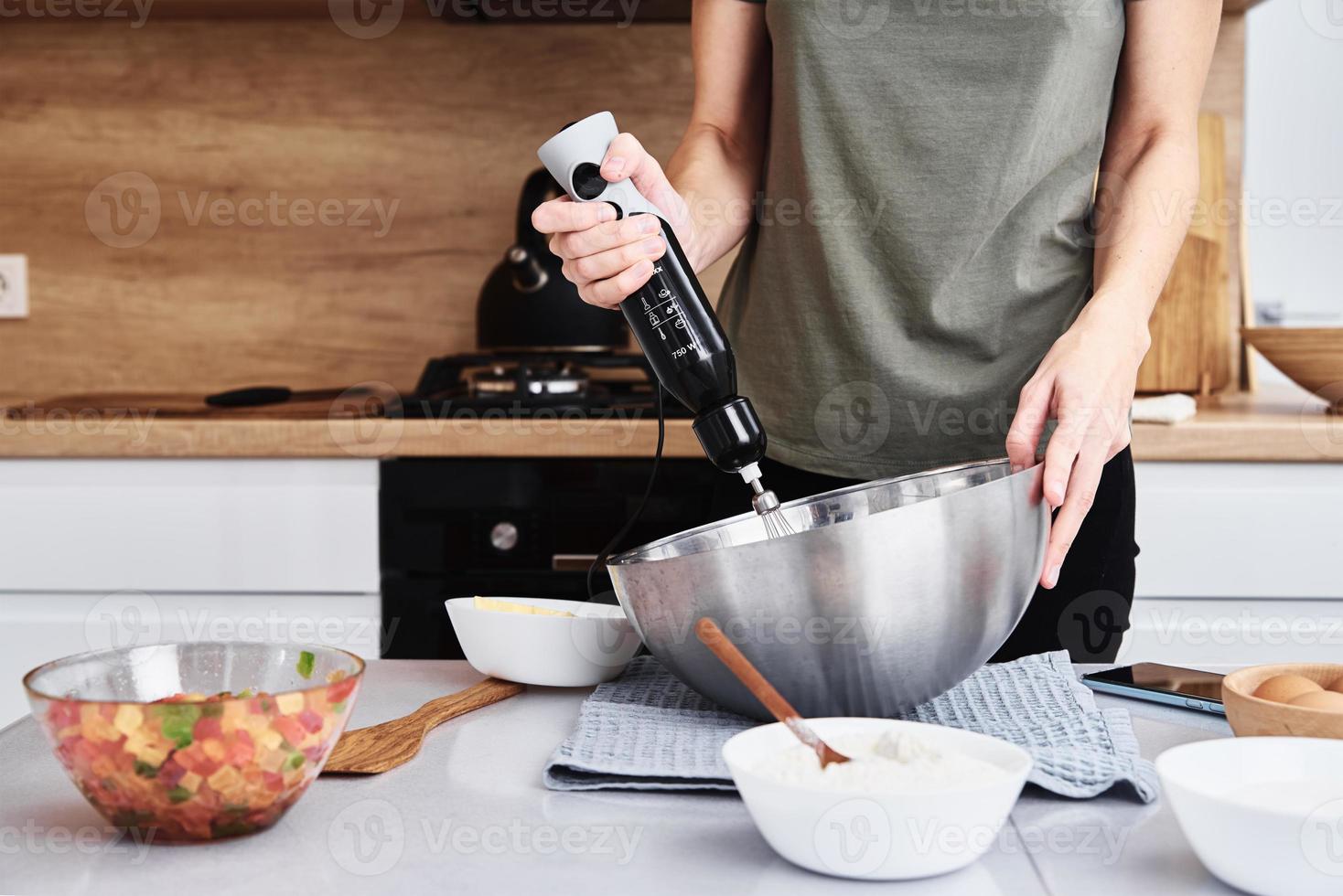 donna nel cucina cucinando un' torta. mani battere il Impasto con un elettrico miscelatore foto