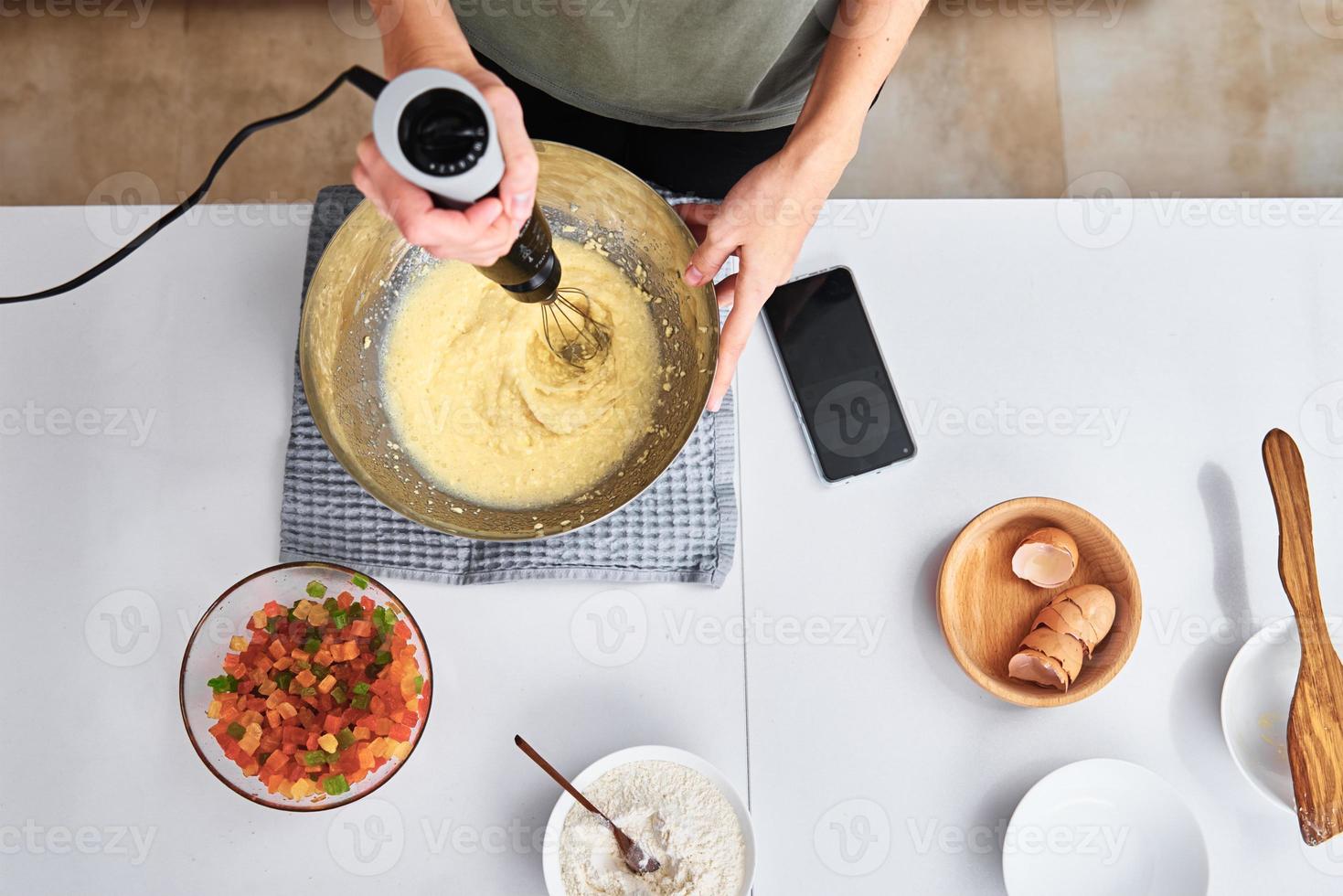 donna nel cucina cucinando un' torta. mani battere il Impasto con un elettrico impastatrice, superiore Visualizza foto