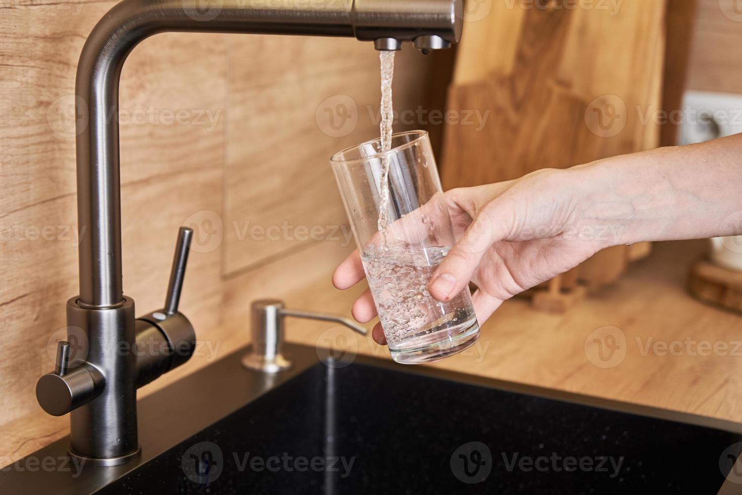 donna versare pulito acqua a partire dal rubinetto filtro in un' bicchiere foto