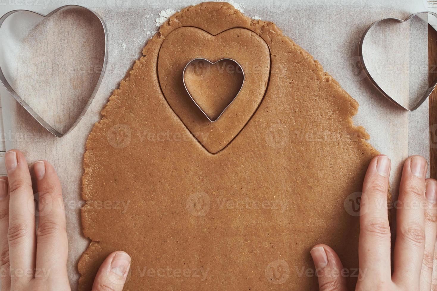 fabbricazione Pan di zenzero biscotti nel il forma di un' cuore per san valentino giorno. donna mano uso biscotto taglierina. vacanza cibo concetto foto